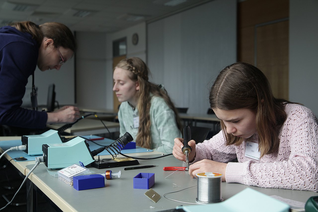 Two girls are soldering components onto small circuit boards.