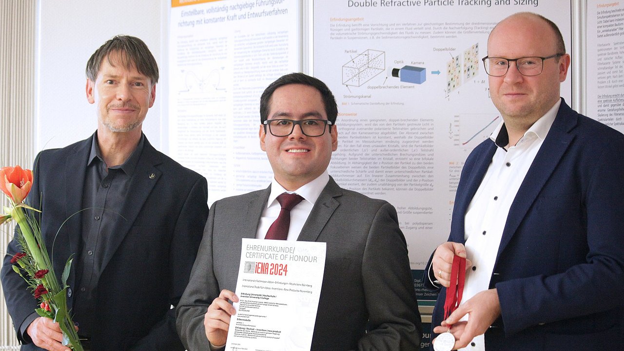 Alex S. Huaman (IMMS, Mitte) am 12.12.2024 zur Thüringer Auszeichnungsveranstaltung des PATON | Landespatentzentrum Thüringen bei der Übergabe der iENA-Silbermedaille durch Sascha Erfurt (PATON, links) und Herrn Könicke (iENA, rechts). Foto: IMMS.