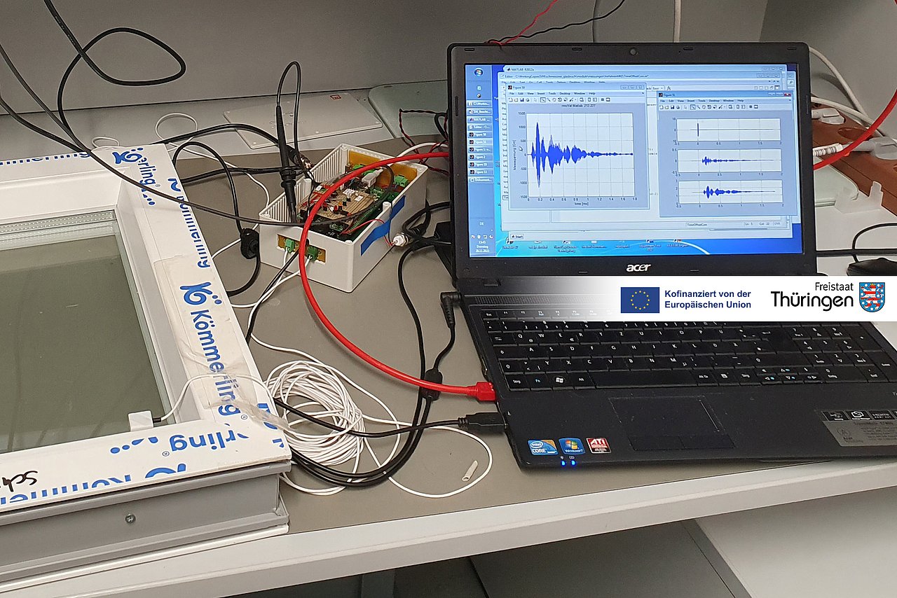 Messaufbau mit Fensterscheibe, Glasbruchsensor, Messgerät und Laptop