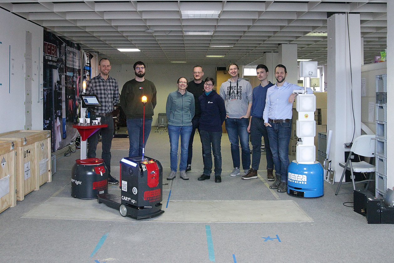 Die Partner von MetraLabs und IMMS zum Kick-off-Treffen des Projekts ERA-AMR am 14.01.2025. In ERA-AMR werden optimierte Antriebssysteme für autonome mobile Roboter erarbeitet. Foto: IMMS. Das Projektteam aus acht Personen steht hinter drei autonomen Robotern.