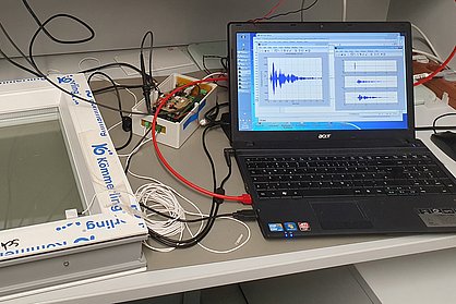 Messaufbau mit Fensterscheibe, Glasbruchsensor, Messgerät und Laptop