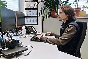 Ein Mann sitzt vor einem Computer mit 2 Bildschirmen mit Programmier- und Entwurfsumgebung. 