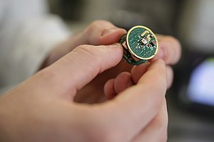 Zwei Hände halten Platinen in der Größe von Euro-Münzen mit einer LED in der Mitte