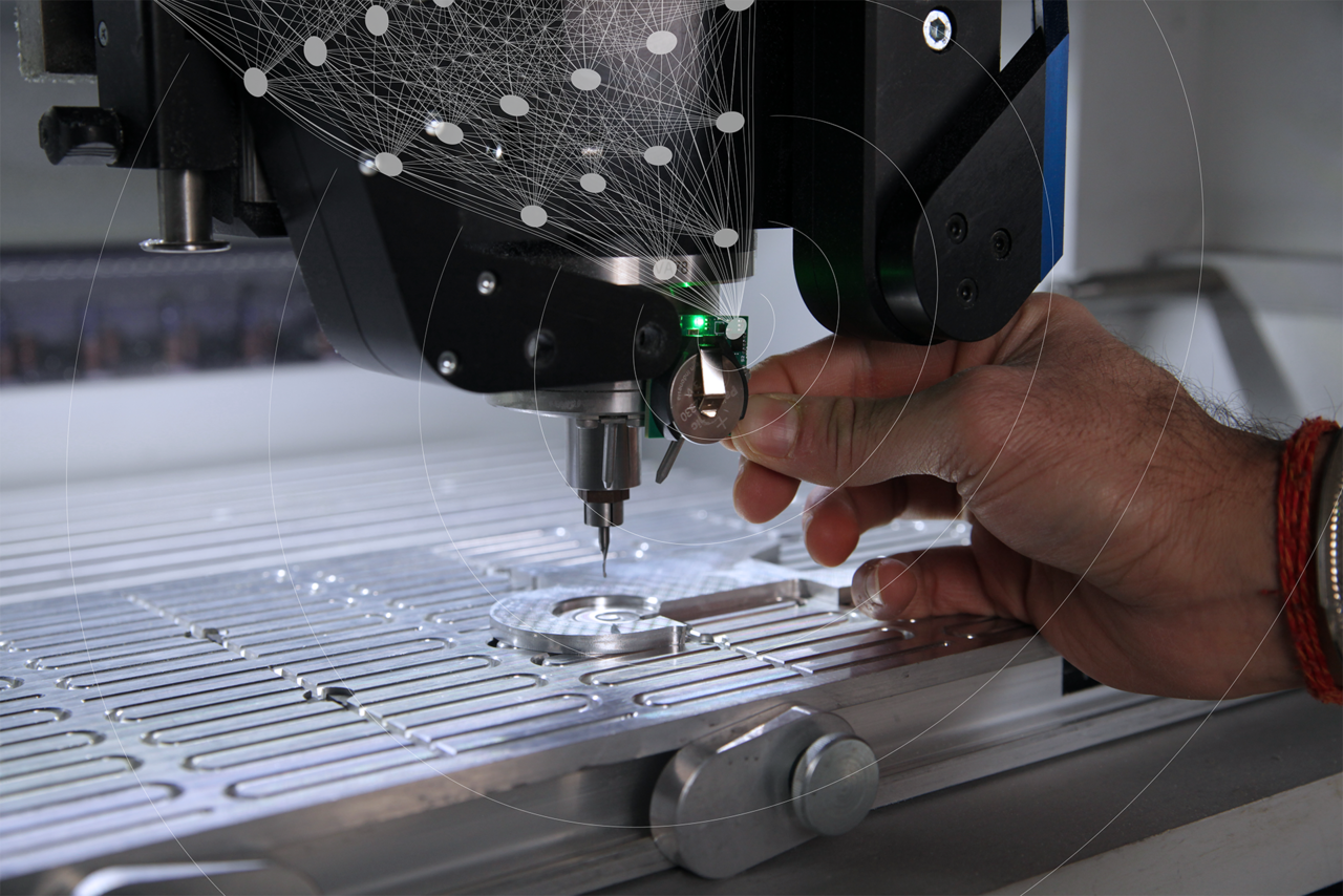 Close-up of a milling machine to which an approximately 2 x 2 cm small wireless circuit board with sensors and an illuminated LED is held, accompanied by a graphic of a neural network and spreading radio waves.