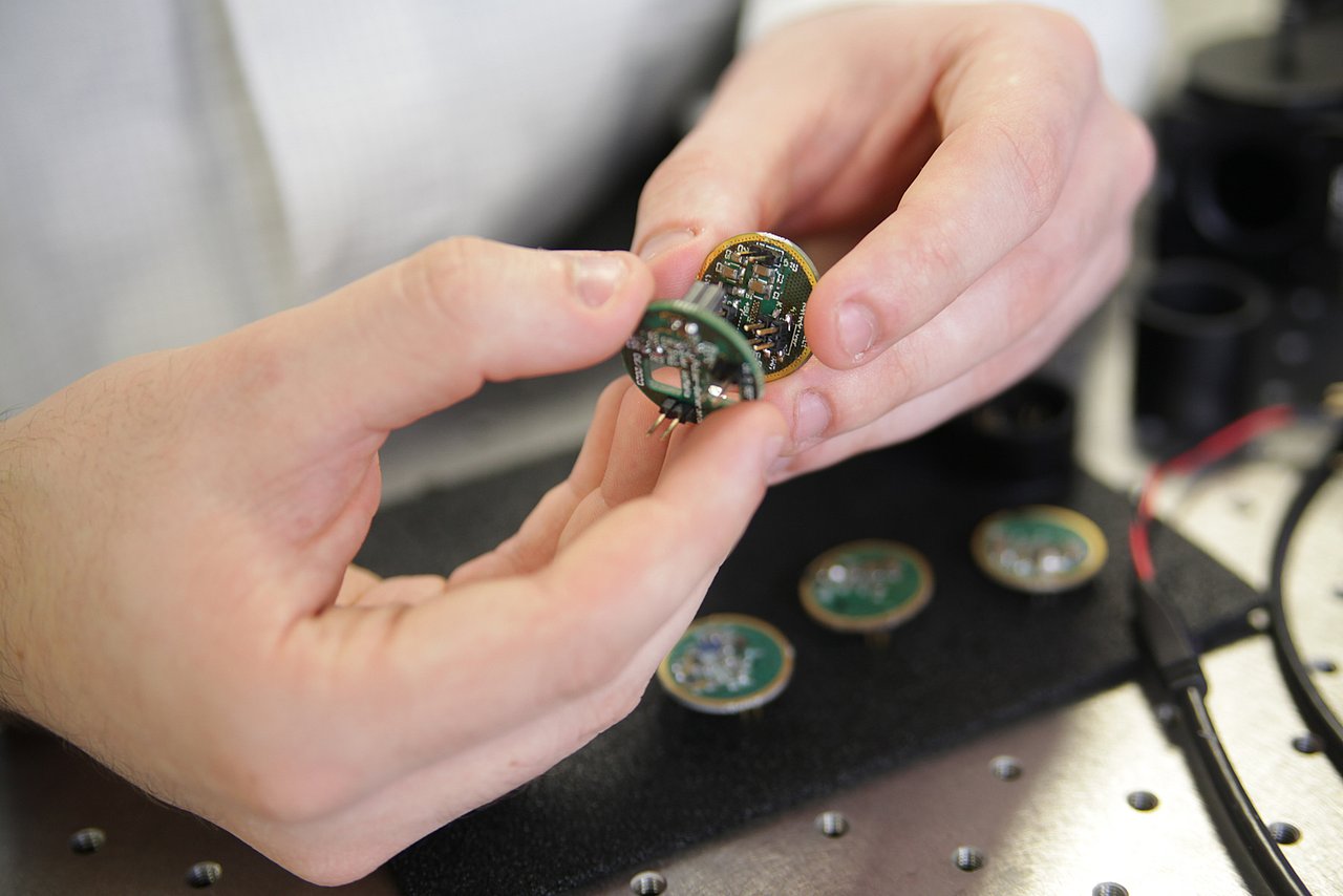 Driver circuit with commercially available LEDs for time-resolved fluorescence measurements in the nanosecond range, enabling new applications in in vitro diagnostics. Photograph: IMMS. Two hands hold two circuit boards approximately the size of euro coins.
