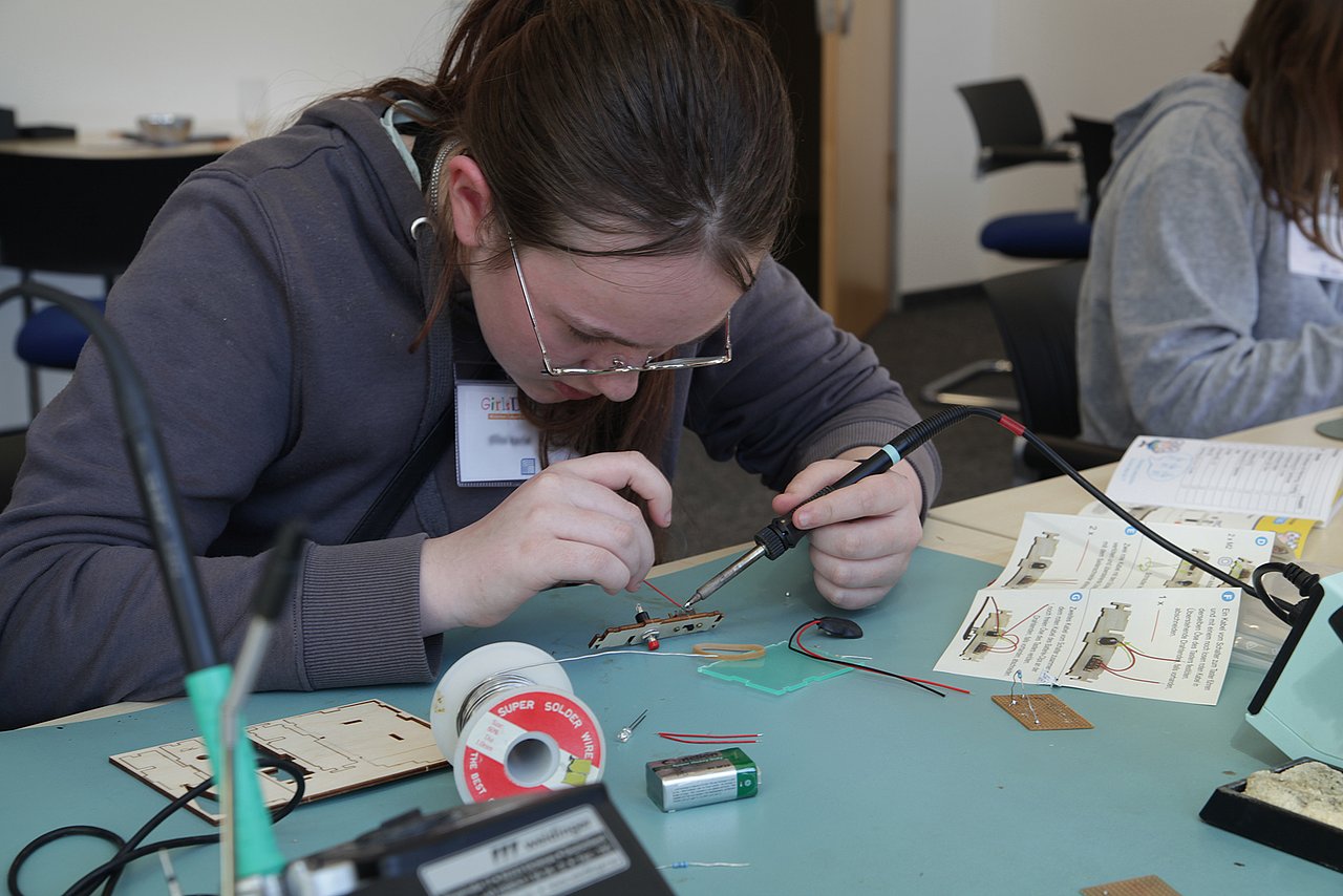 Ein Mädchen sitzt am Tisch und lötet an einer Platine.