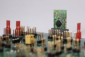 Eine kleine Platine mit vergossenem Chip, die im 90-Grad-Winkel in einer großen Platine steckt. 