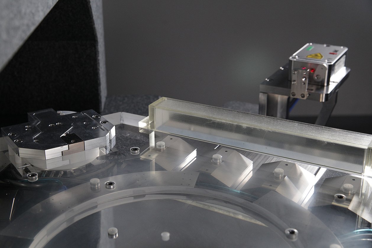 NPS6D200 – 6D-controlled direct drive system  for nanometre-precise positioning in the motion range of Ø 200 mm x 25 mm  Close-up of the quartz glass slider with a metal lifting module, magnetic bridges and laser interferometer.