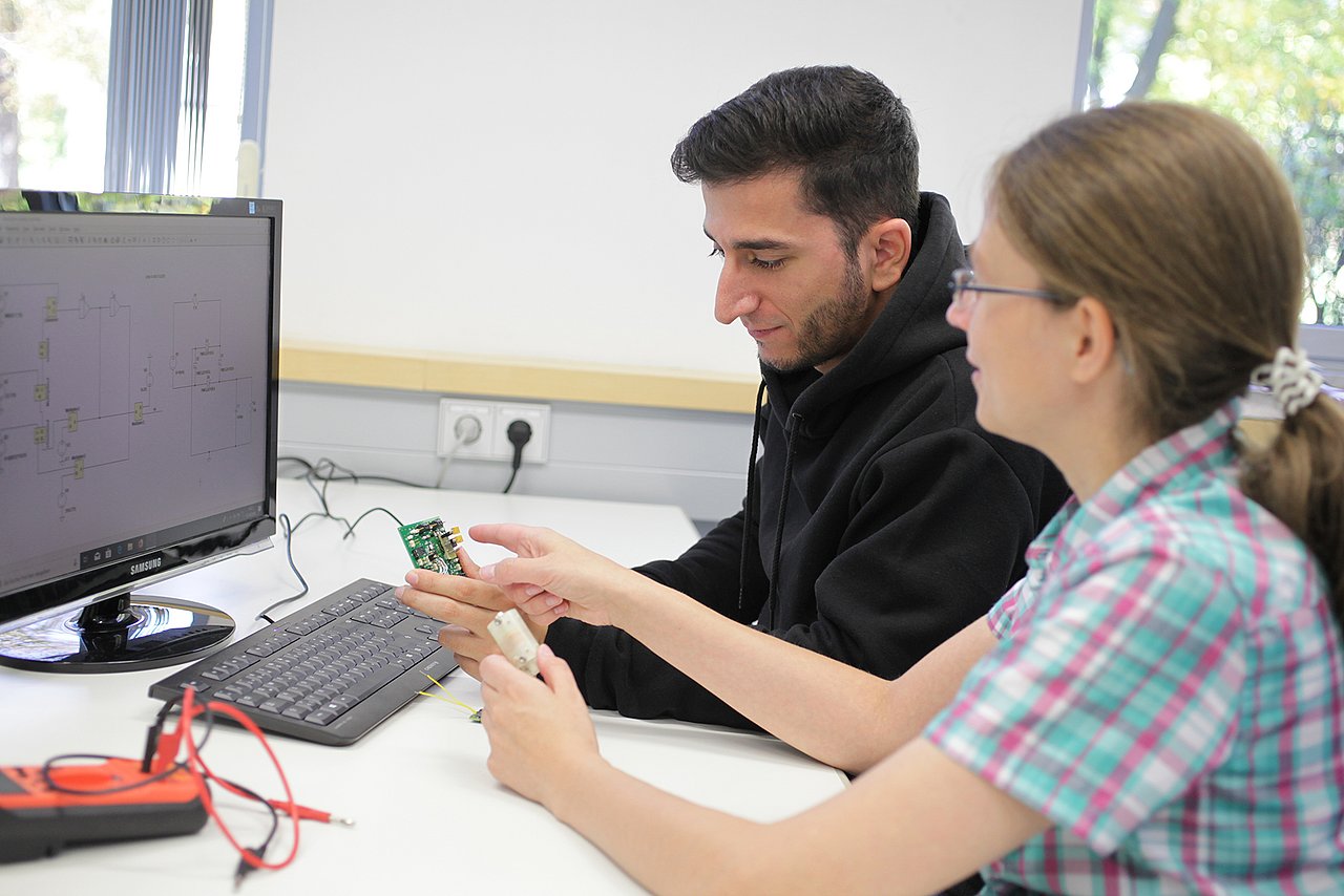 Zwei Mitarbeiter des IMMS sitzen an einem Rechner und prüfen einen elektronischen Testaufbau.  