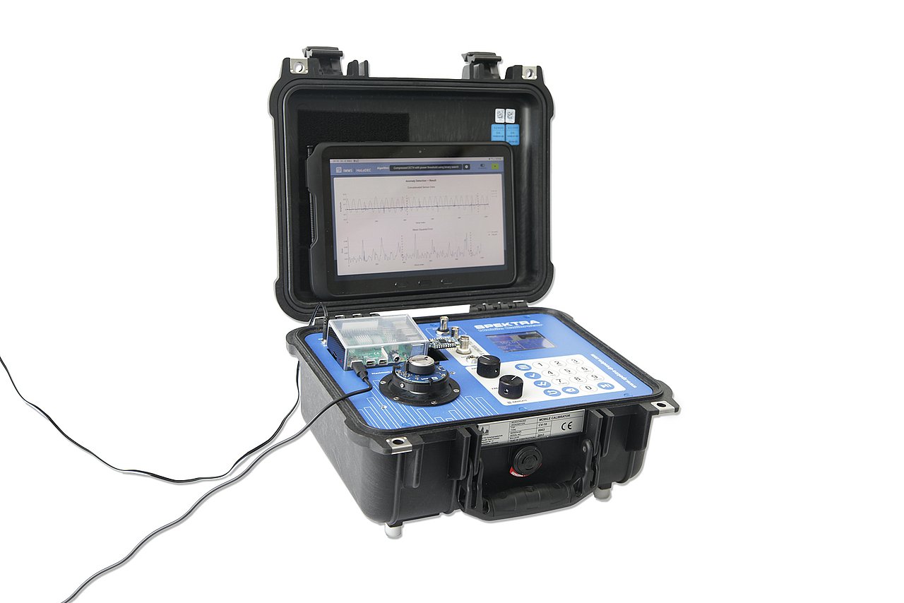 Demonstratorsystem mit  Vibrations­erzeuger in Kofferform, drahlosen Sensorknoten (kleine runde Platine), Edge-Device (größere Platine) und Tablet